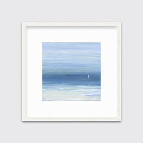 A blue, beige and white abstract seascape print with a small sailboat in a whitewashed frame with a mat hangs on a white wall.