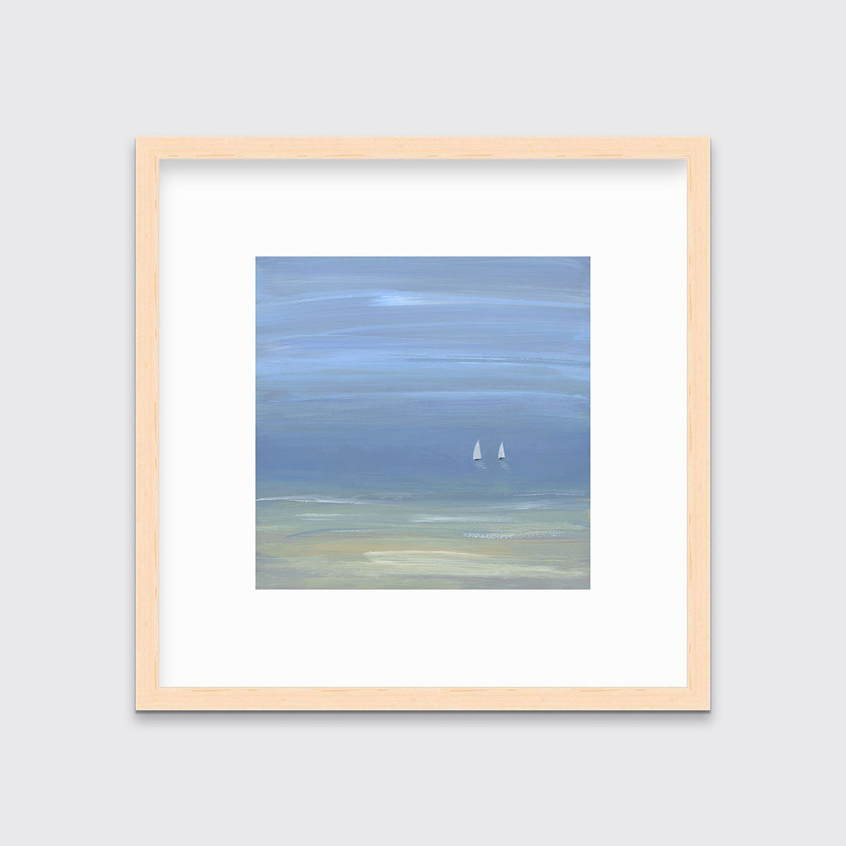 A blue, beige and white abstract seascape print with two small sailboats in a natural wood frame with a mat hangs on a white wall.