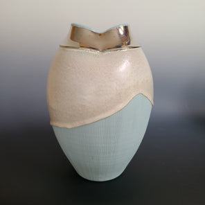 A turquoise vase dipped in a pearl colored glaze, with a white gold luster around the mouth of the vessel. Sits infront of a grey background.