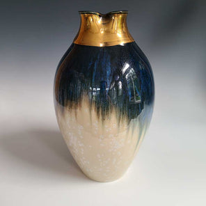 A dark blue and cream crystalized glazed vase with a gold fluted opening sits on a white surface.