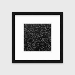 A black and grey abstract print in a black frame with a mat hangs on a white wall.