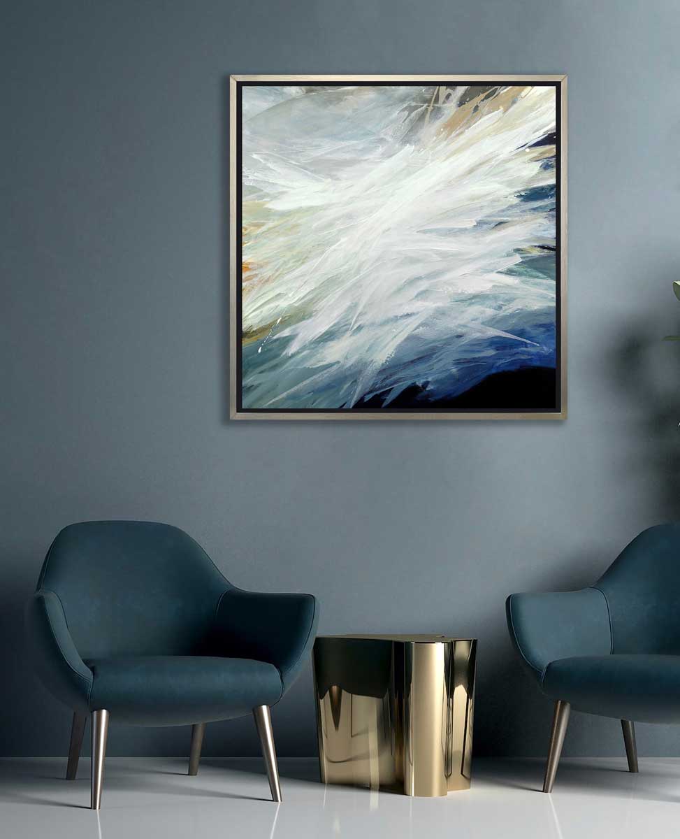 A blue, teal, beige and white abstract print in a silver floater frame hangs on a dark teal wall above two deep teal chairs and a gold art side table.