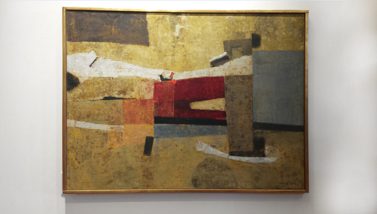 A brown abstract painting in a gold frame hangs on a white wall.