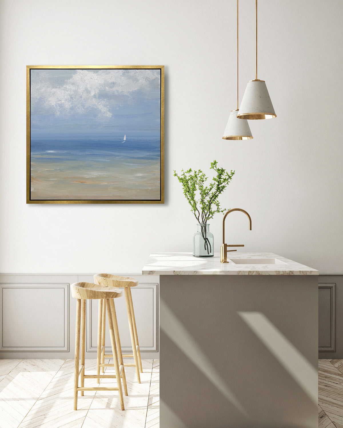 A blue, light green, beige and white abstract seascape print with a small sailboat in a gold floater frame hangs on a white wall above a white marble kitchen island with a sink and a clear glass vase with greenery stems and two wood counter stools.