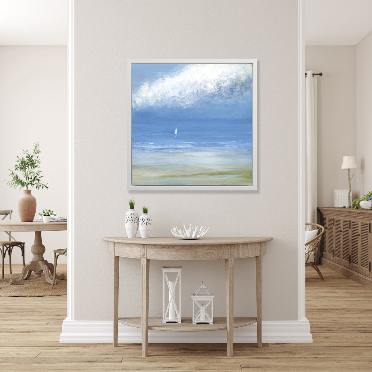 A blue, light green and white abstract seascape print with a small sailboat in a white floater frame hangs on a white wall above a raw wood half circle console table with two white vases, a white decorative bowl and two white lanterns.