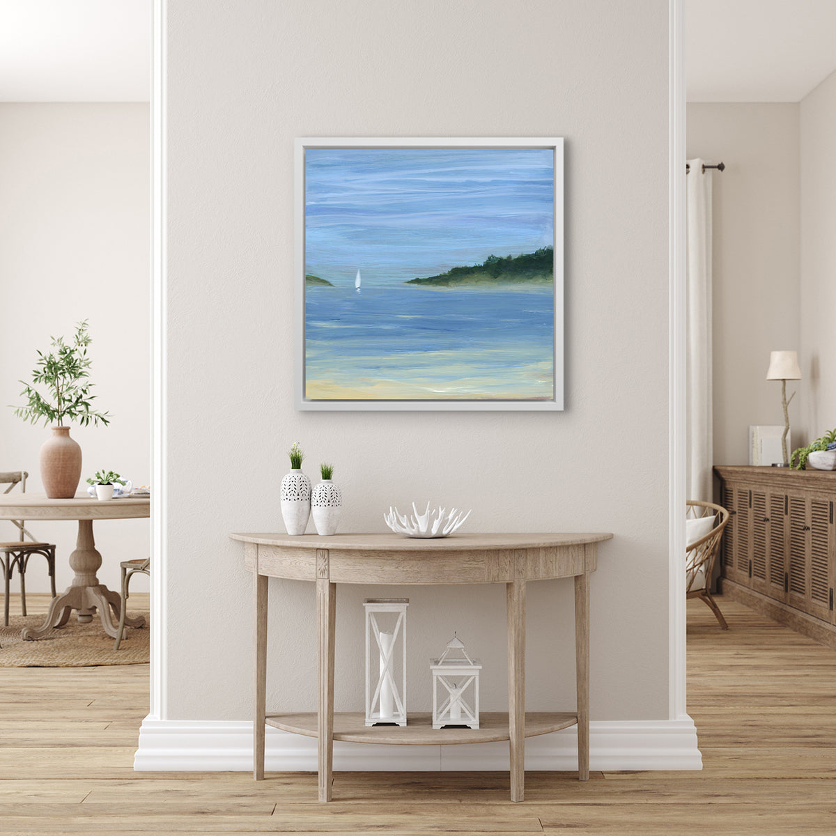 A blue, green and white abstract seascape print with a small sailboat in a white floater frame hangs on a white wall above a raw wood half circle console table with two white vases, a white decorative bowl and two white lanterns.