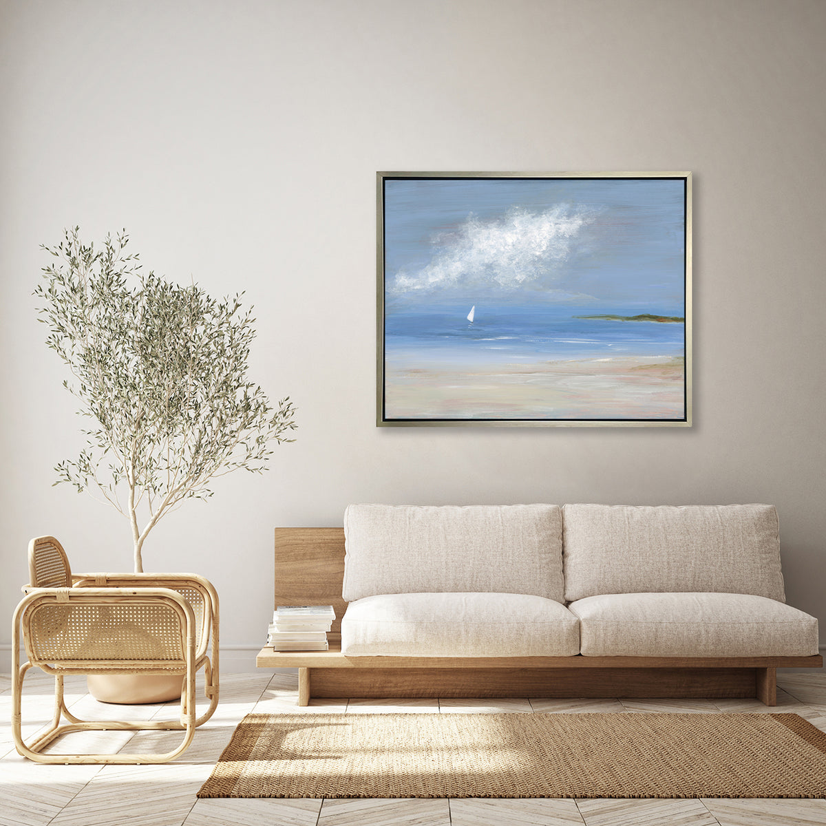 A blue, beige and white abstract seascape print with a small sailboat in a silver floater frame hangs on a white wall above a wood base with cushions, a taupe rug and a modern bamboo chair.