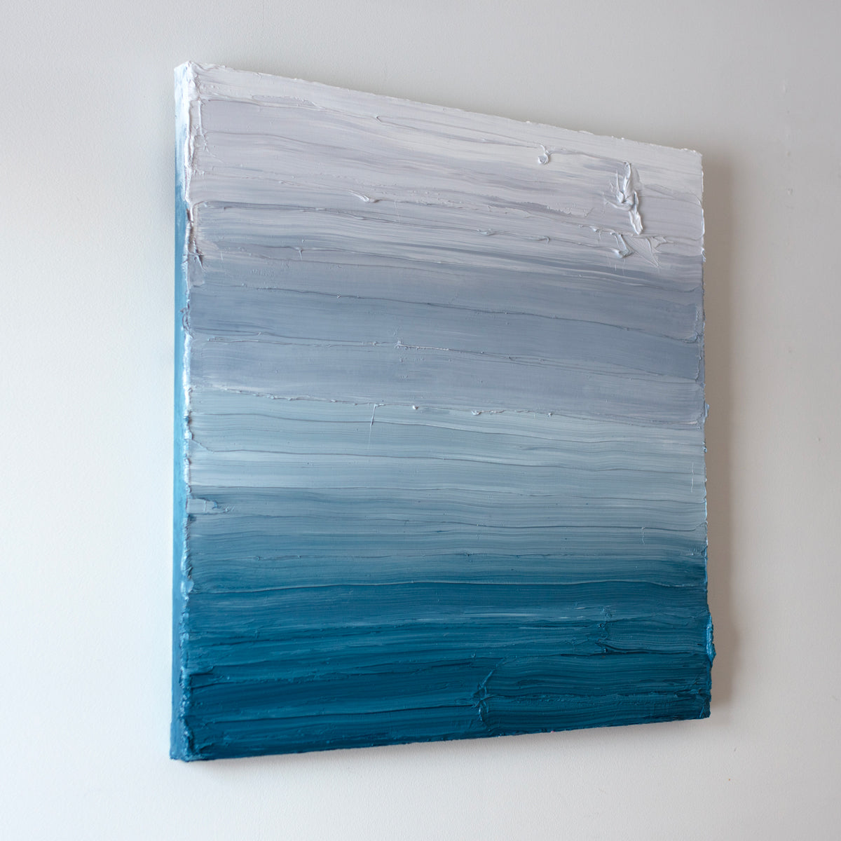 A left side-view of a white, light grey and tonal blues abstract painting by Teodora Guererra hangs on a white wall.