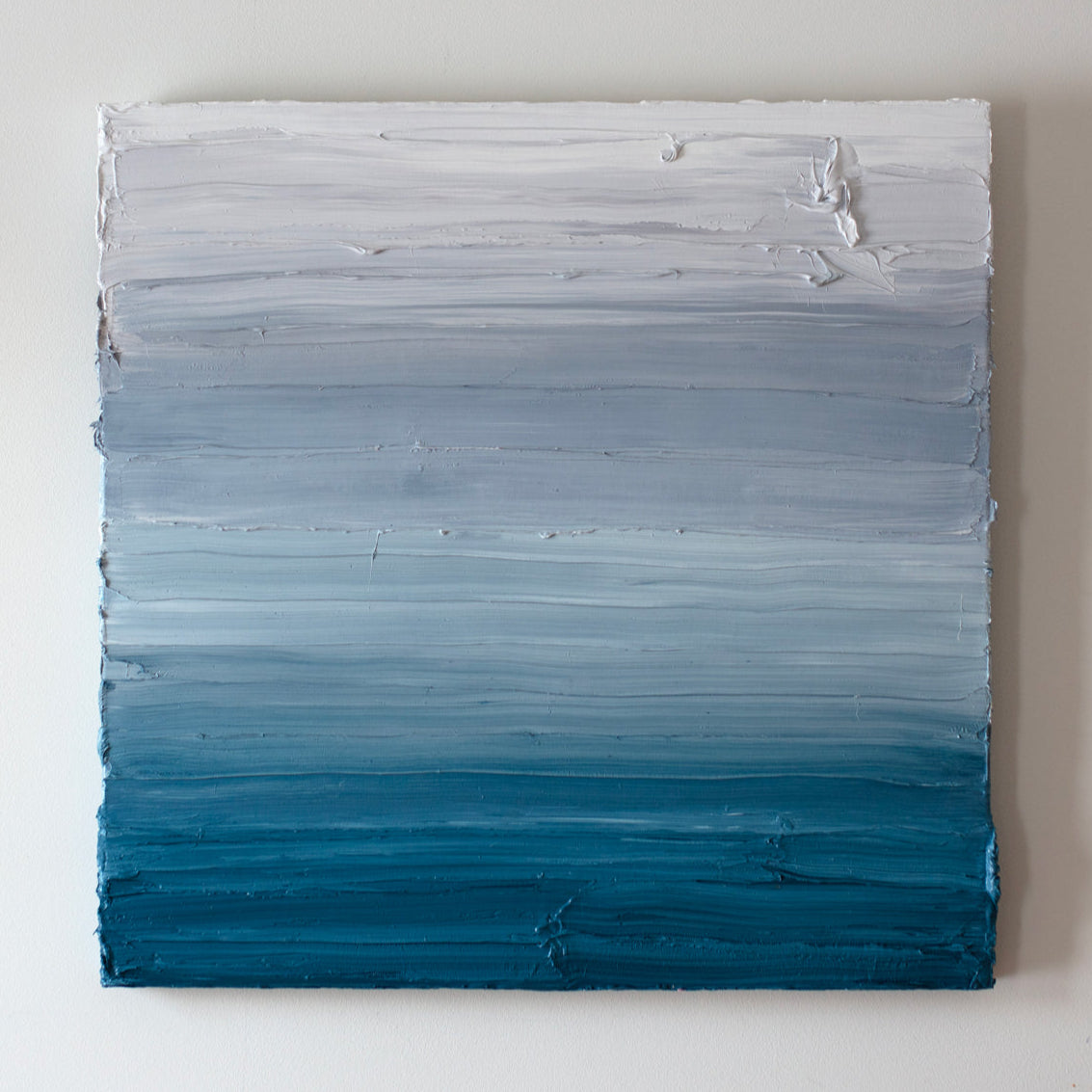 A white, light grey and tonal blues abstract painting by Teodora Guererra hangs on a white wall.