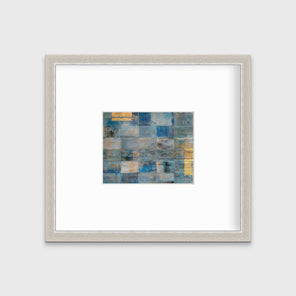 A blue and gold geometric abstract print in a silver frame with a mat hangs on a white wall.