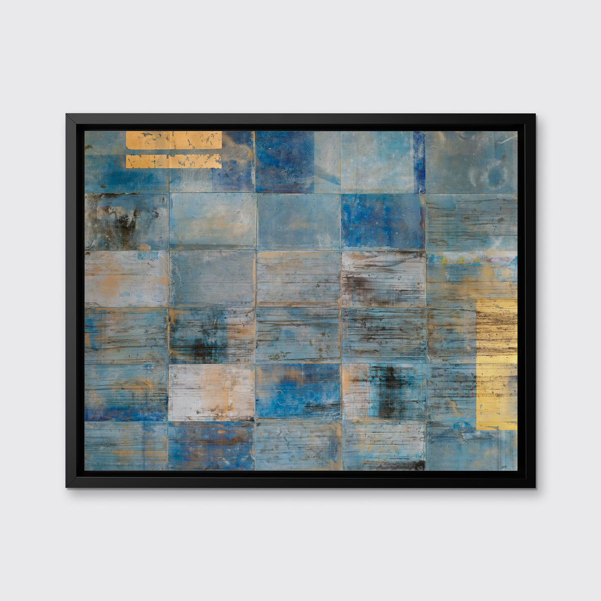 A blue and gold geometric abstract print by Ned Martin hangs in a black floater frame on a white wall.