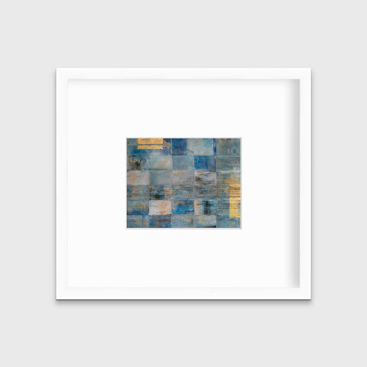 A blue and gold geometric abstract print in a white frame with a mat hangs on a white wall.