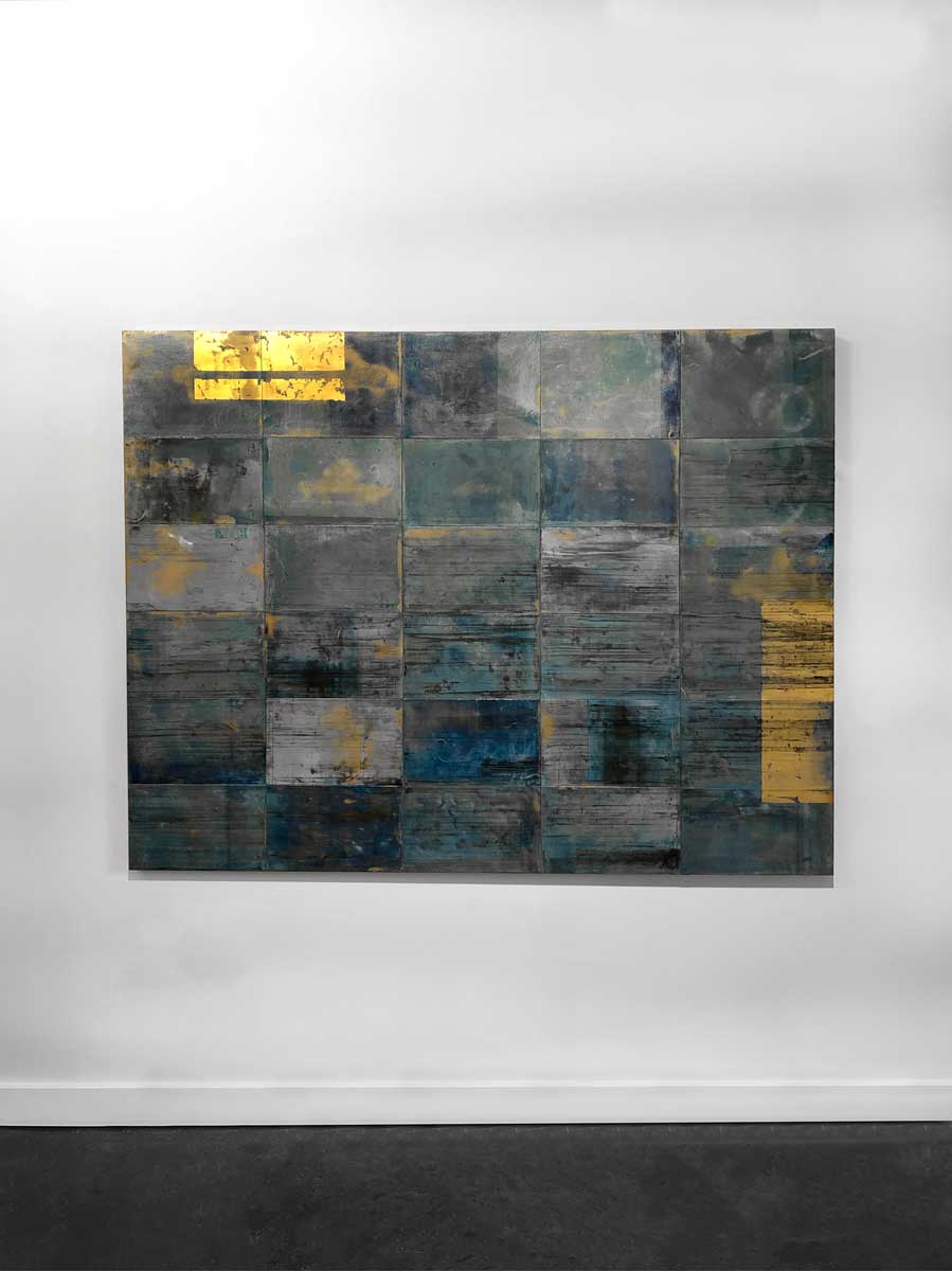 A blue, light blue and gold geometric abstract painting hangs on a white wall.