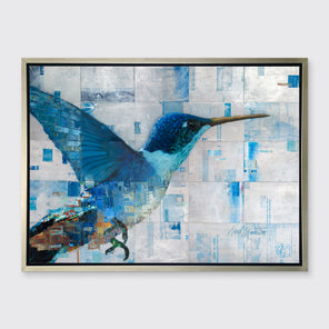 A blue and silver geometric abstract print of a hummingbird in a silver floater frame hangs on a white wall.