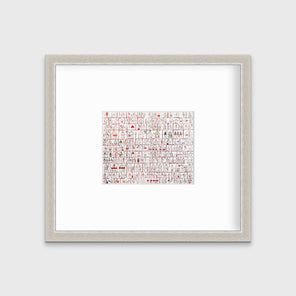 A red and white abstract house print in a silver frame with a mat hangs on a white wall.