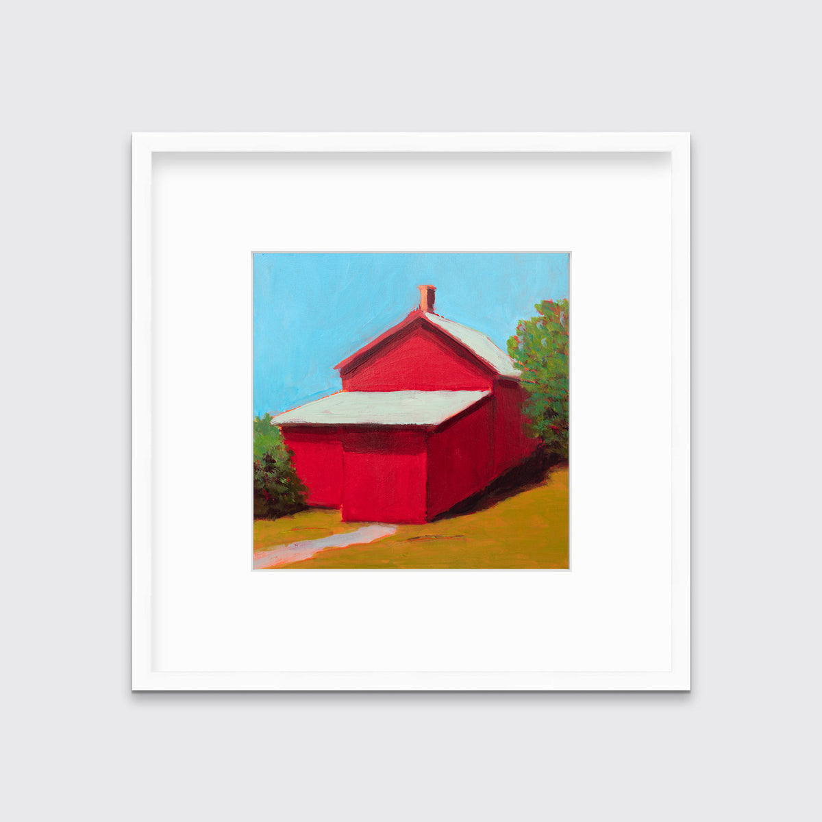 A print of a red barn with a grey roof, blue sky, green bushes and a chartreuse lawn in a white frame with a mat hangs on a white wall.