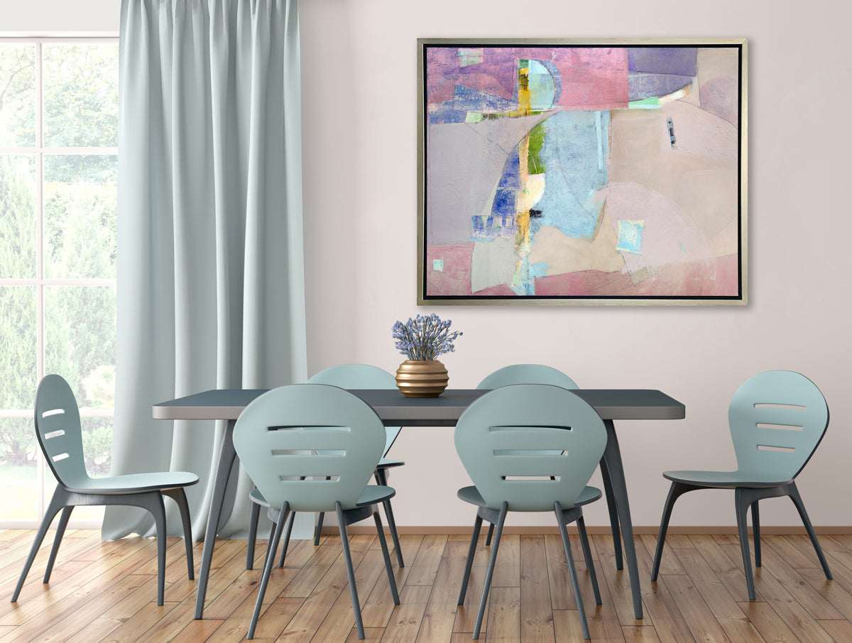 A pink, light blue, green and purple abstract print in a silver floater frame hangs on a white wall above a dark teal table with a purple floral arrangement in a gold vase and six light teal chairs.