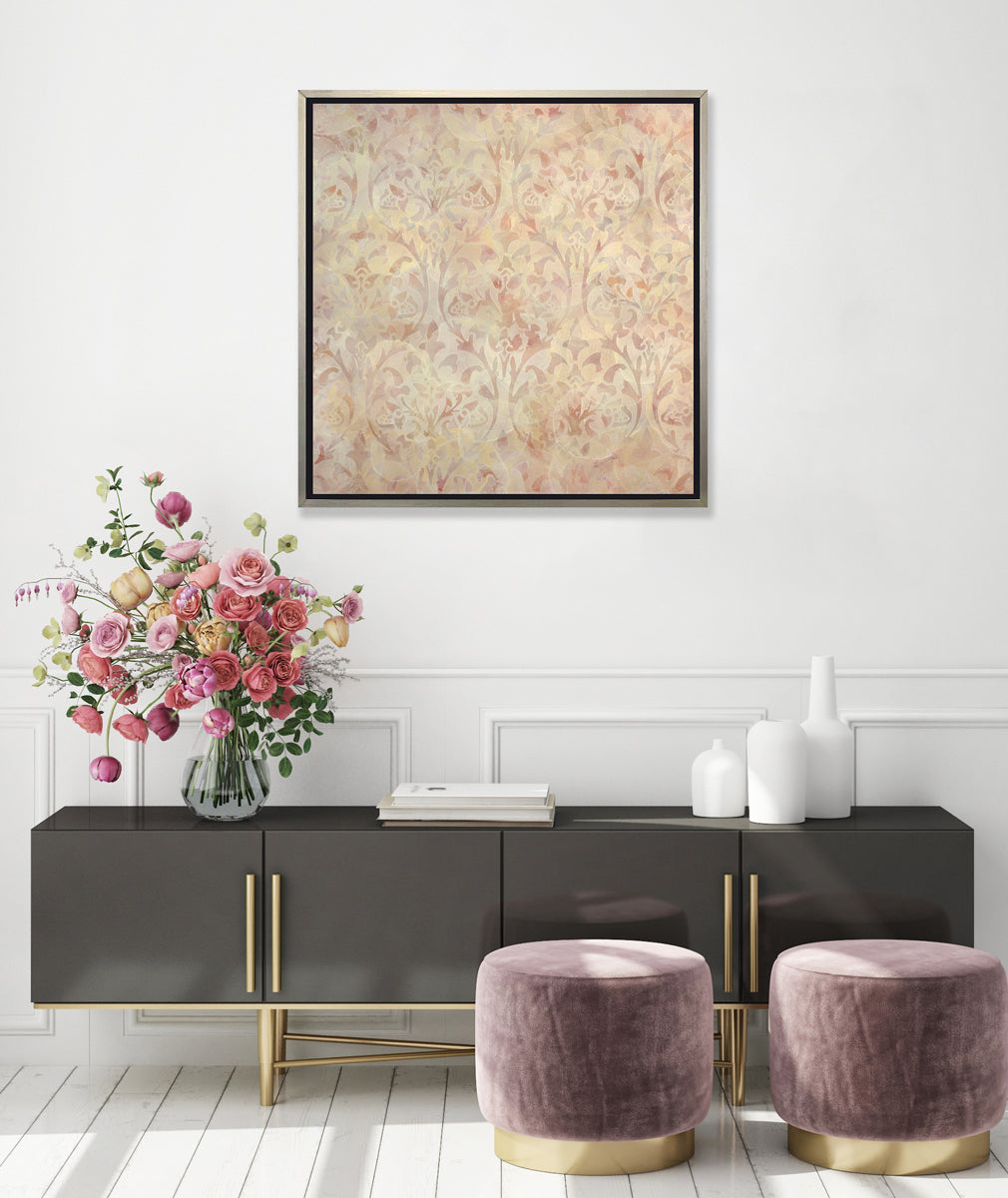 A pale pink and pale yellow abstract print in a silver floater frame hangs on a white wall above a black sideboard cabinet with white vases, a stack of books, a clear vase with a large floral arrangement and two mauve ottomans on the floor.