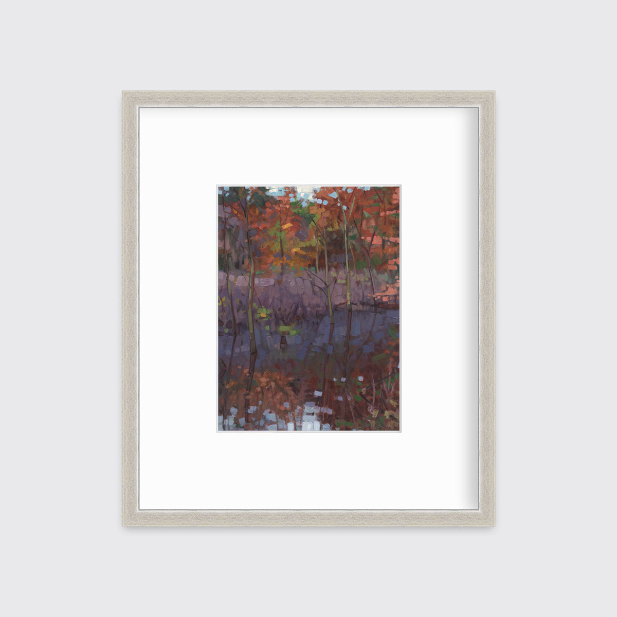 A muted multicolored abstract landscape print in a silver frame with a mat hangs on a white wall.