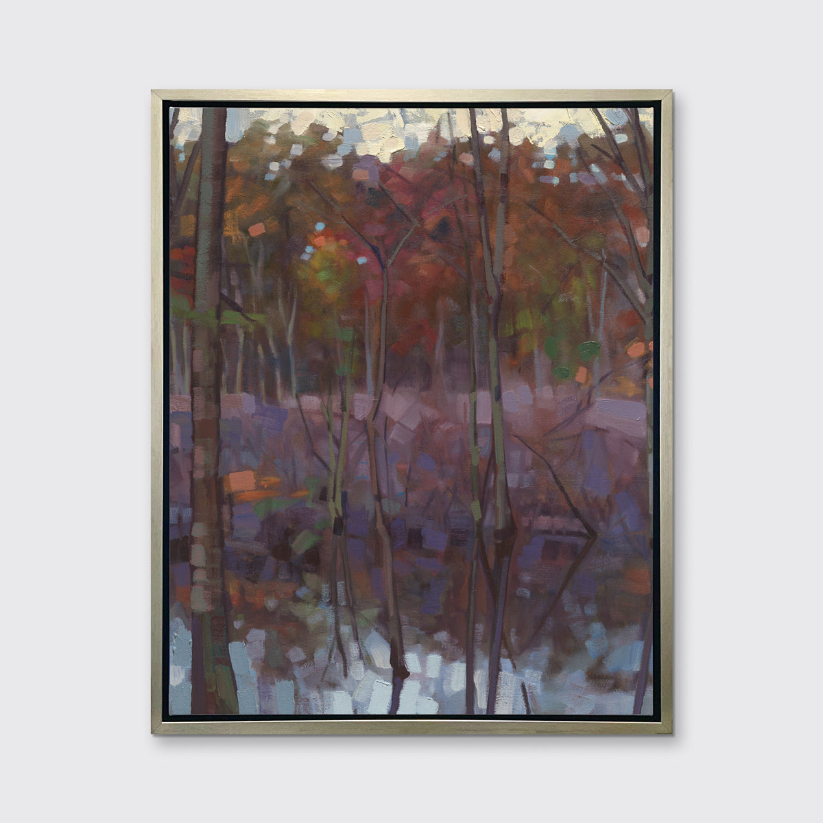 A muted multicolored abstract landscape print in a silver floater frame hangs on a white wall.