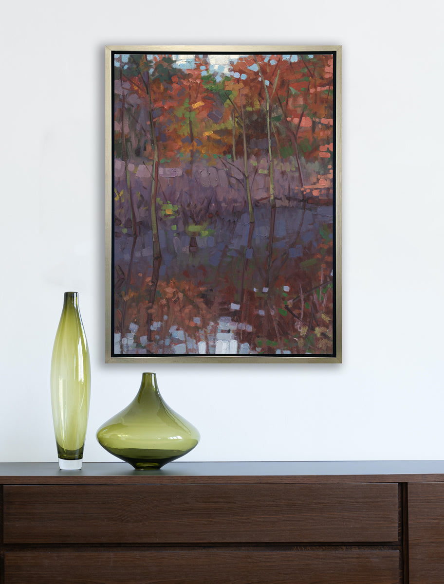 A muted multicolored abstract landscape print in a silver floater frame hangs on a white wall above a dark wood console table with two various sized green glass vases.