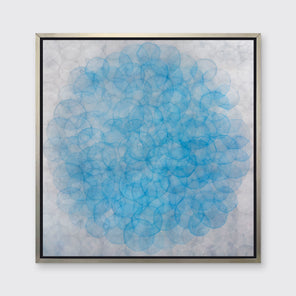 A silver and blue abstract geometric print in a silver floater frame hangs on a white wall.