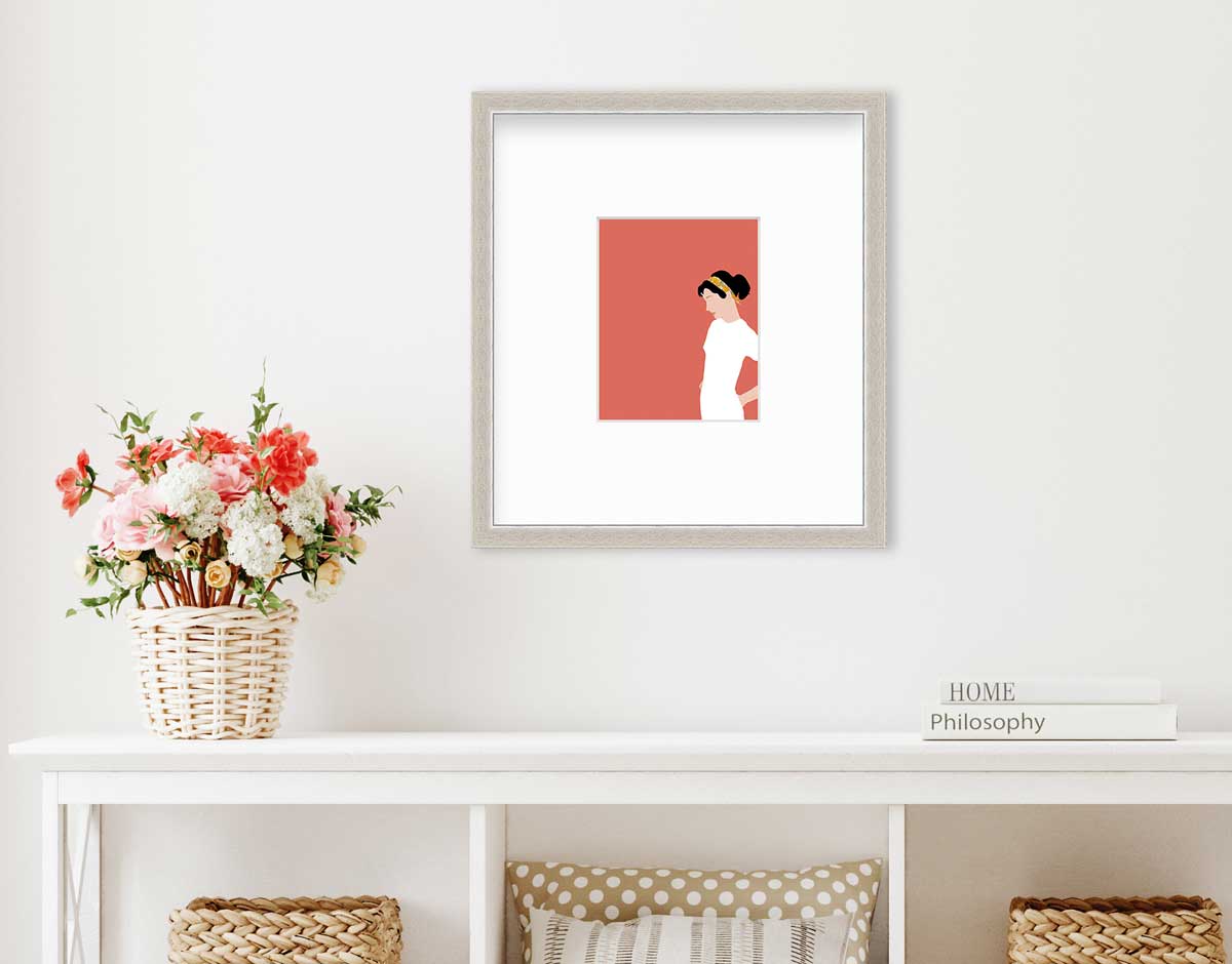 A print with a woman in a white dress and pink background, matted and framed in a silver frame on a white wall above a white console table with white coffee table books stacked to the right and flowers in a wicker basket to the left. 