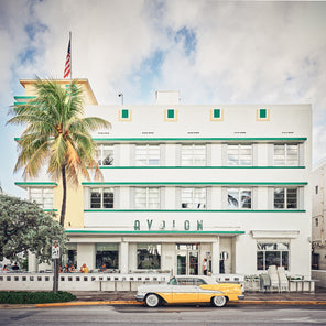 A photograph of an art deco building in Miami Beach with a yellow vintage car and trees. 