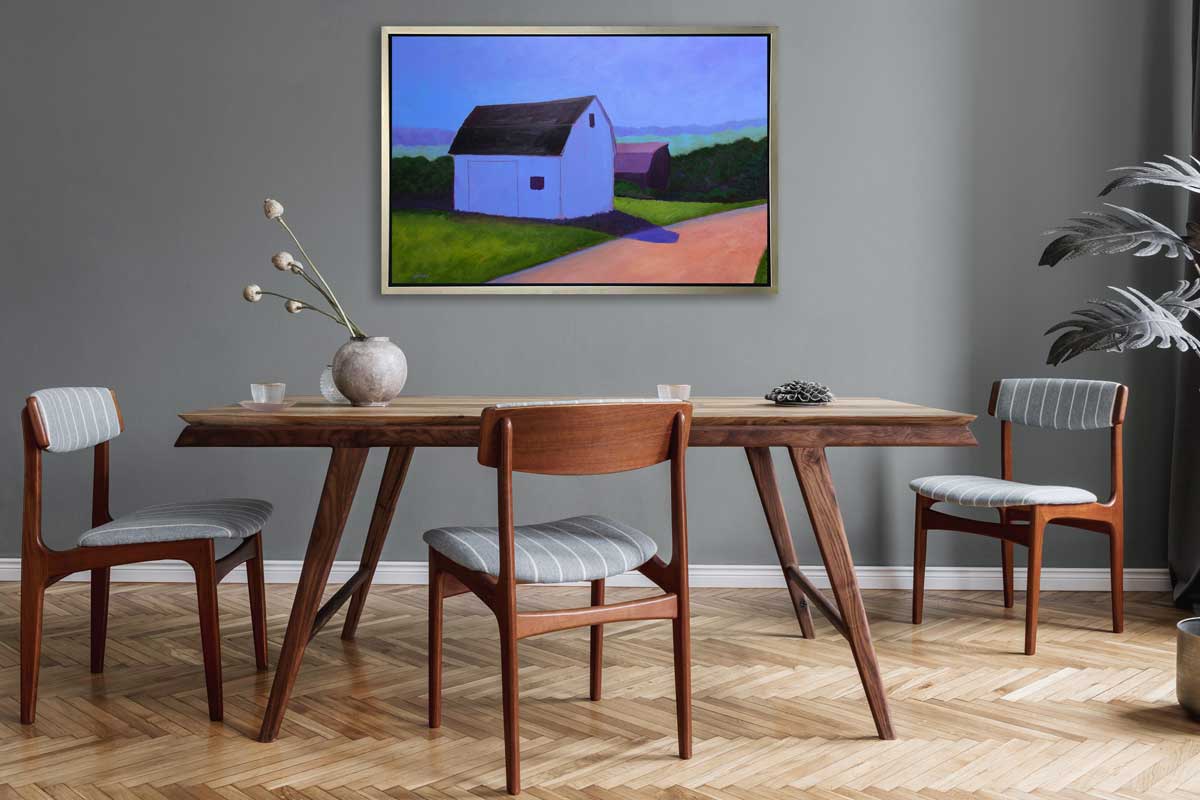 A blue, green and peach contemporary barn print in silver floater frame hangs on a grey wall above a natural wood table with a vase with floral stems and three wood and grey chairs.