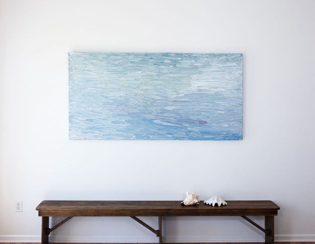 A abstract painting with blue textured brushstrokes is hung above a bench with sea shells on it.