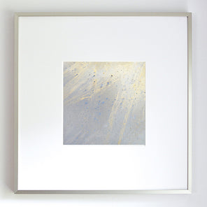 A small light yellow, light blue and silver painted art mirror in a silver frame with a large white mat hangs on a white wall.