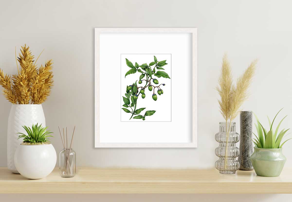 A green plant print in a whitewashed frame with a mat hangs on a white wall above a wood counter with six different vases, some with green plants and some with wheat stems.