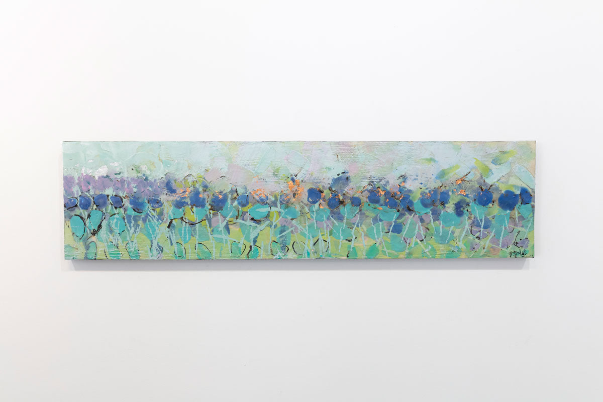 A wooden panel decorated in blue and cyan encaustic markings is hung on a gallery wall.