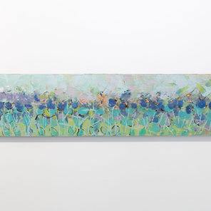 A wooden panel decorated in blue and cyan encaustic markings is hung on a gallery wall.