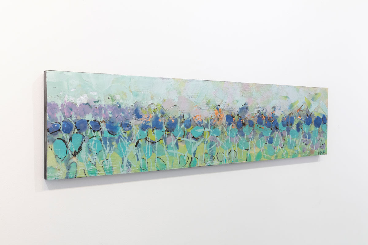 A wooden panel decorated in blue and cyan encaustic markings is seen at an angle on a gallery wall.