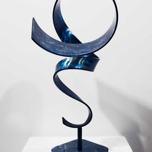 Close up of abstract, steel sculpture with blue dye sitting on a pedestal in front of a white wall.