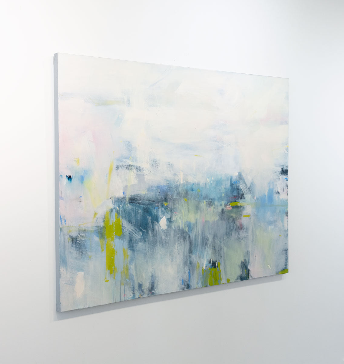 An abstract painting with energetic blue and yellow brushstrokes painted by Kelly Rossetti is seen at an angle on a gallery wall. Wired and ready to hang.