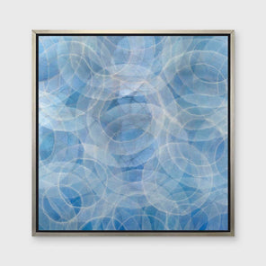 A blue and white abstract geometric print in a silver floater frame hangs on a white wall.