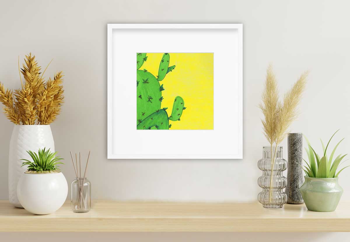 A print of a lime green cactus in front of a vibrant yellow background in a white frame with a mat hangs on a white wall above a natural wood shelf with a variety of potted plants to the left and right. 