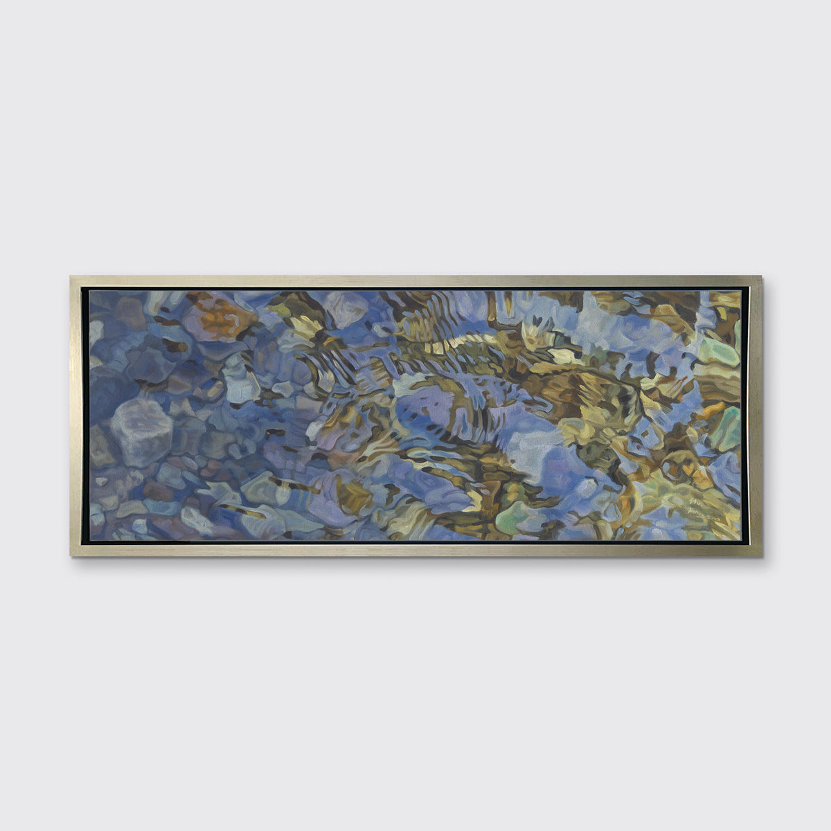 A brown, dark green, white and light blue abstract river rocks in water print in a silver floater frame hangs on a white wall.