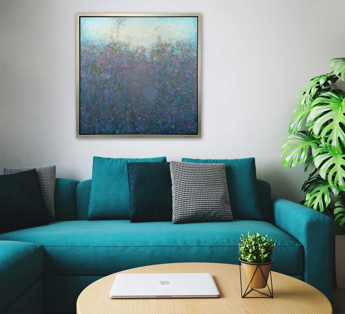 A blue and purple abstract landscape print in a silver floater frame hangs on a white wall above a teal sofa with pillows, a wooden round coffee table and a potted floor plant.