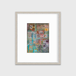 A multicolored abstract print in a silver frame with a mat hangs on a white wall.