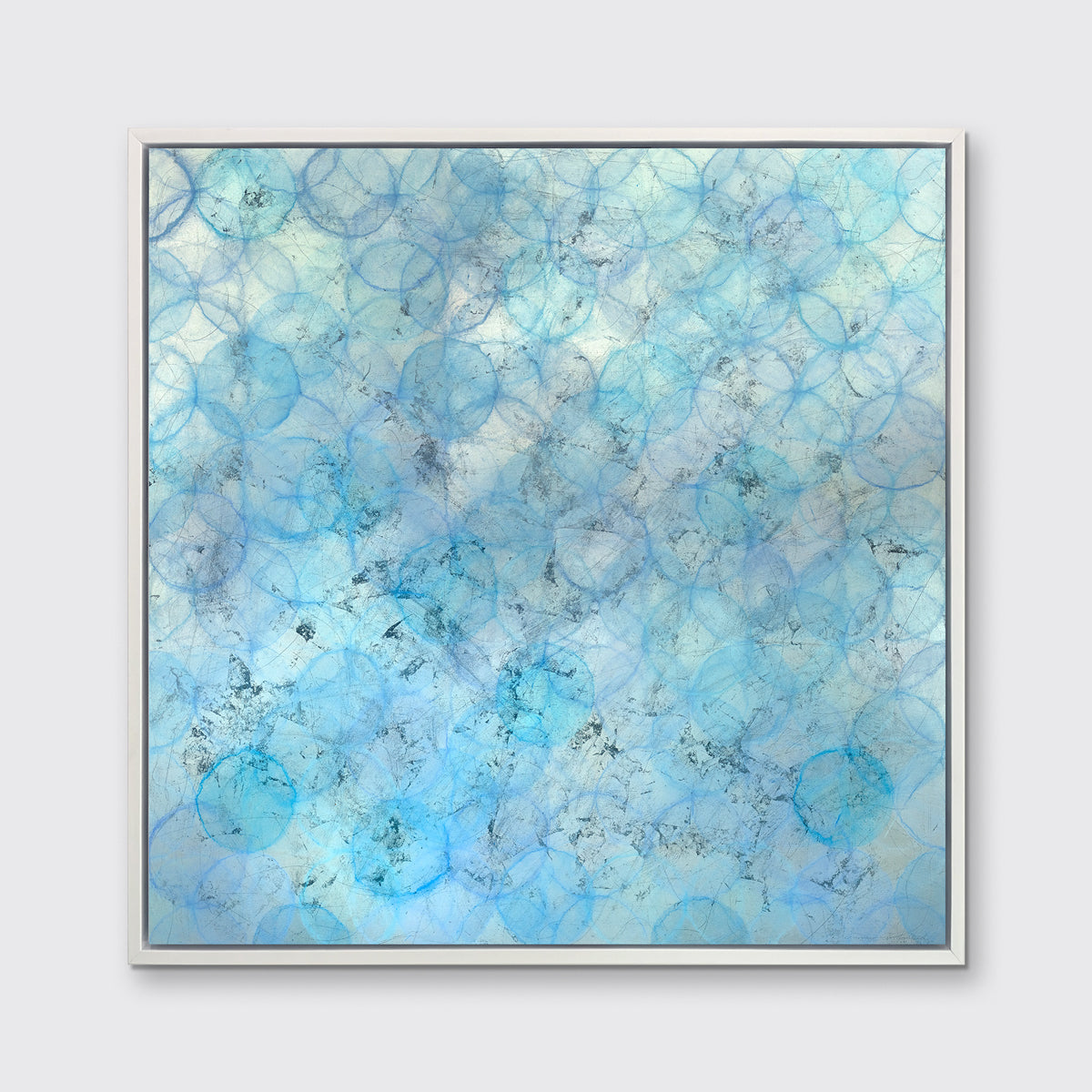 A blue and silver abstract circle print in a white floater frame hangs on a white wall.