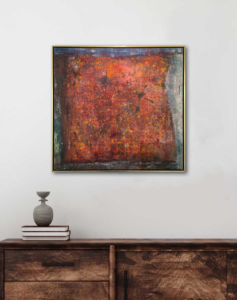 A red, orange and grey abstract painting in a warm gold frame hangs on a white wall above a stained wood cabinet with three stacked books and a small grey vase.