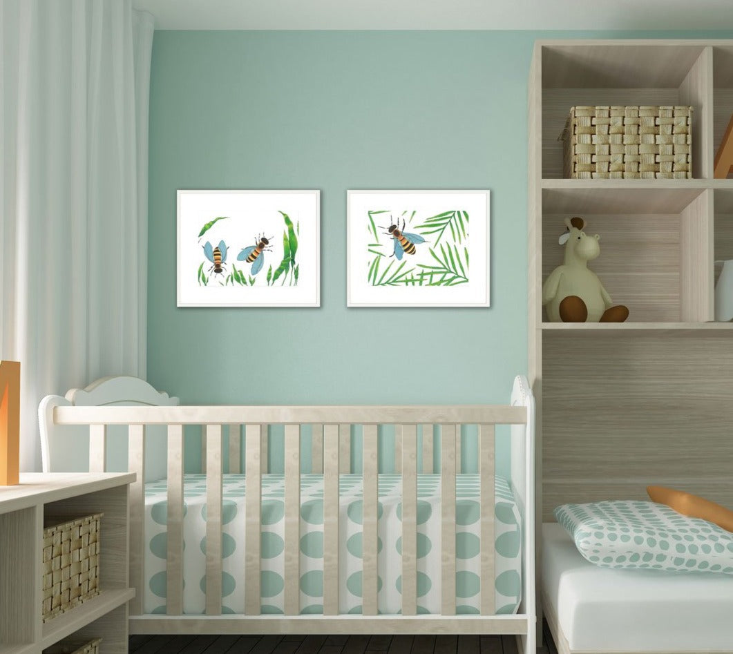 Two white and green bee illustration prints by Elizabeth Iadicicco in a white frame with a mat hangs on a light blue wall in a baby's room above a the light grey wood crib with polka dot bedding.