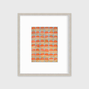 A orange, white and light blue abstract circle print in a silver frame with a mat hangs on a white wall.