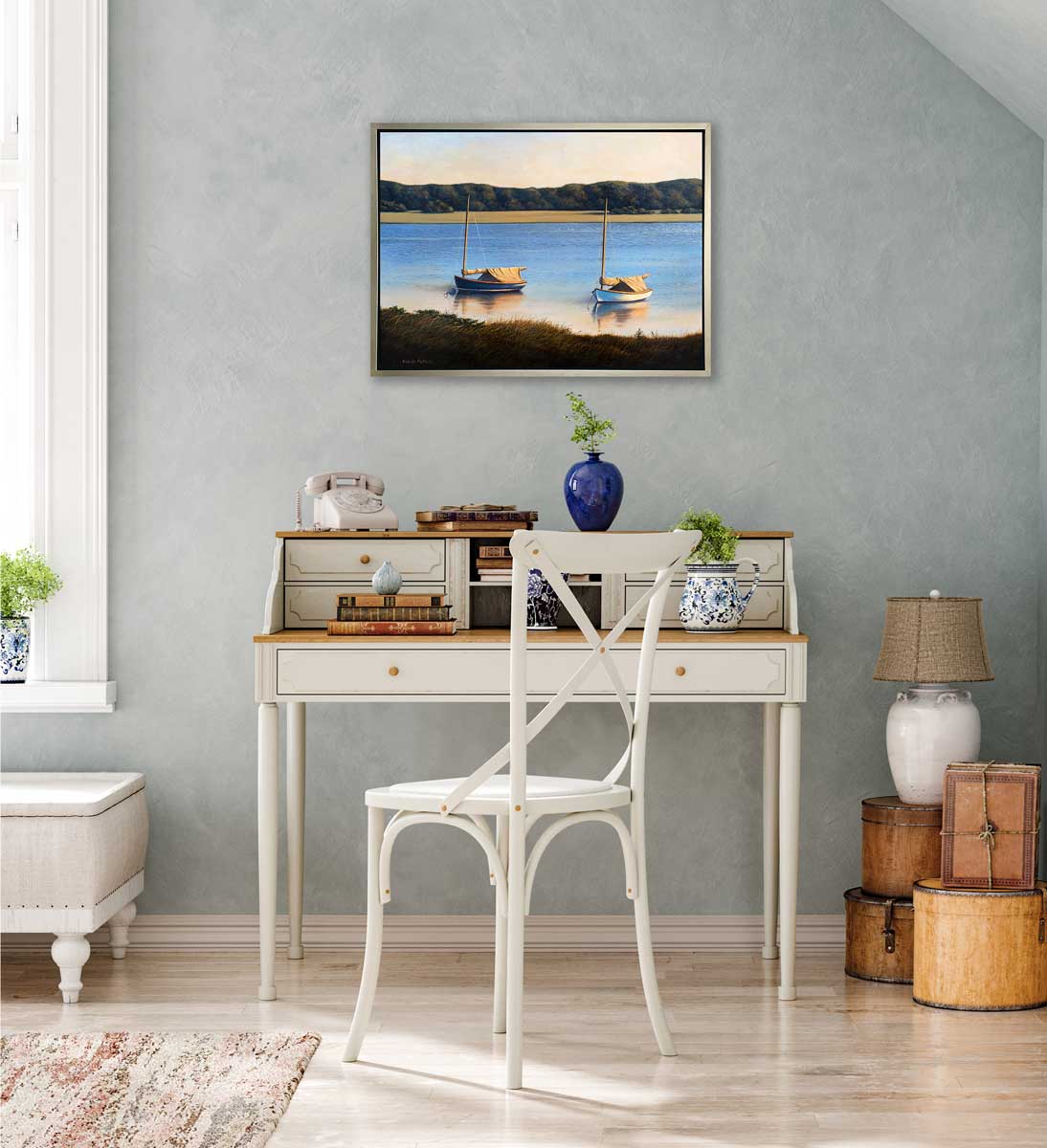 A contemporary realist print of two anchored boats wading in the water in a silver floater frame hangs on a textured light teal wall above a two tiered white desk with accessories and a white chair.