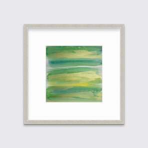 A green, blue and gold abstract print in a silver frame with a mat hangs on a white wall.