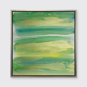 A green, blue and gold abstract print in a silver floater frame hangs on a white wall.
