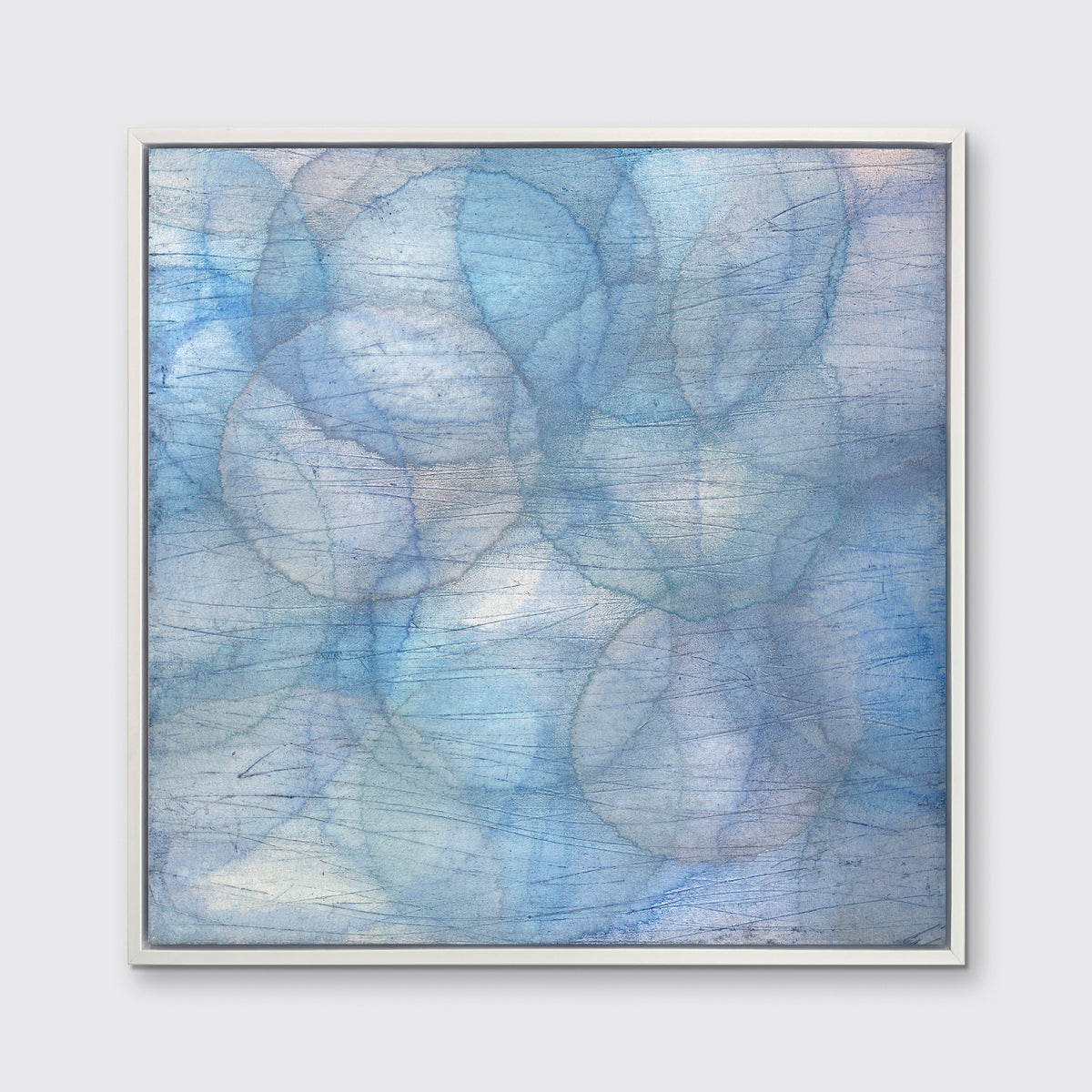 A blue, teal and light purple overlapping circle print in a white floater frame hangs on a white wall.
